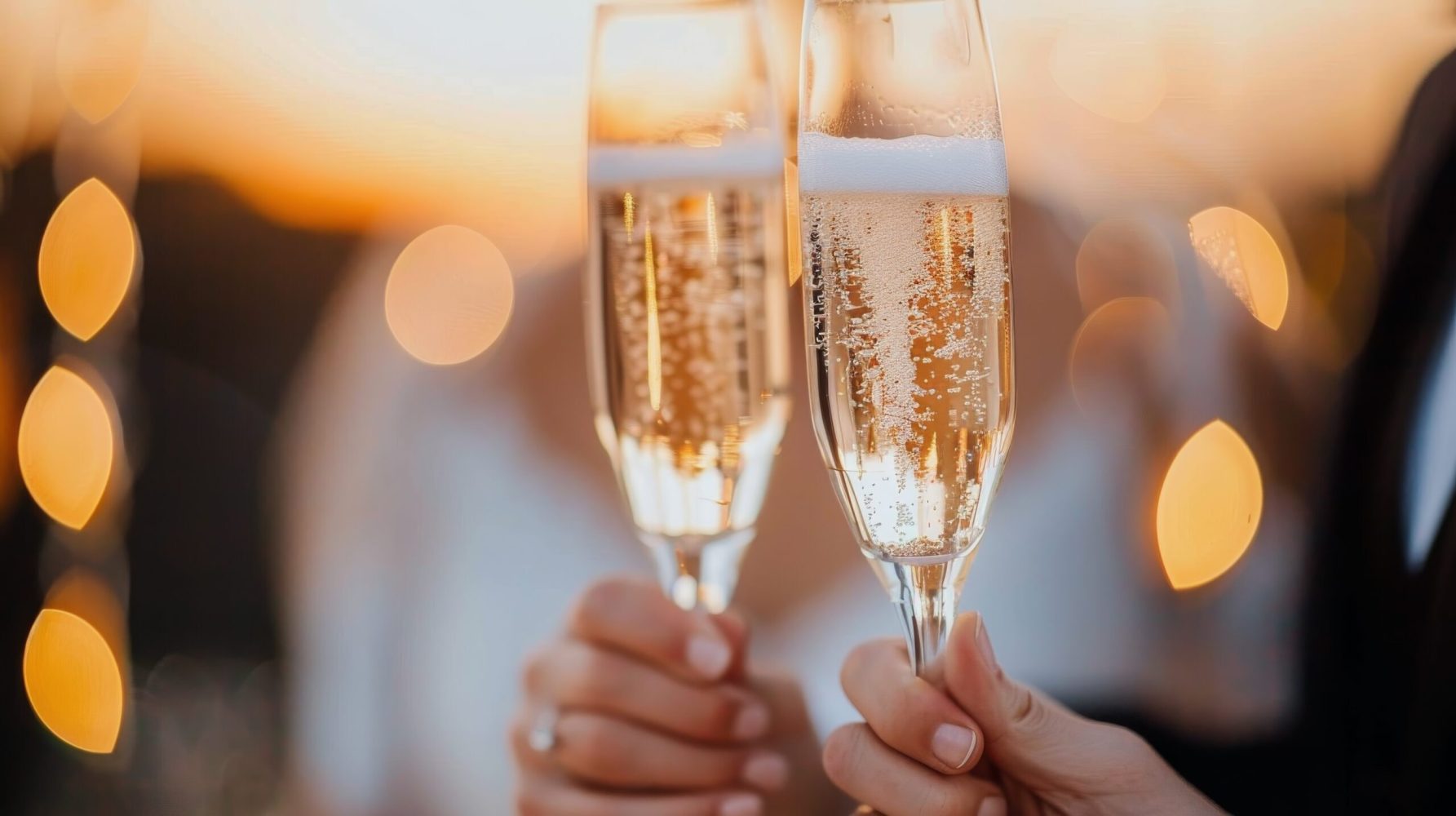 A joyful couple clinks their champagne glasses together, celebrating their union. The bride holds a delicate bouquet of roses, while the setting captures the spirit of their outdoor wedding.